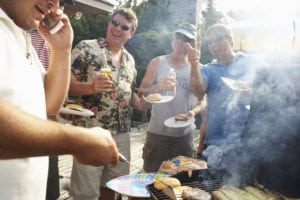 Man barbecuing using mobile phone, friends laughing in background